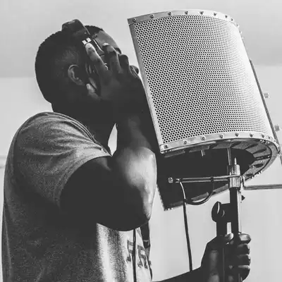 Black-and-white photo of a man in headphones singing into a microphone behind a reflection screen