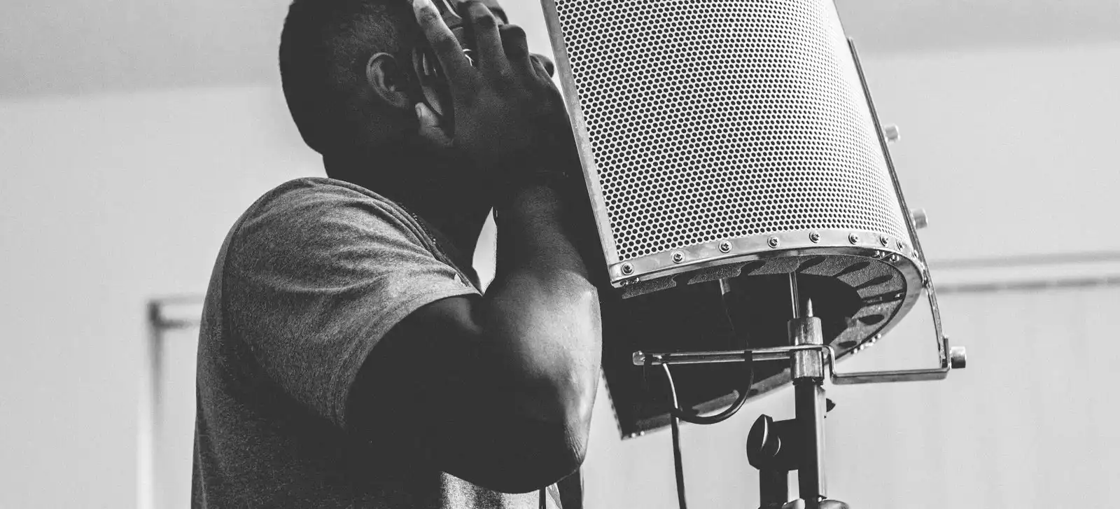 Black-and-white photo of a man in headphones singing into a microphone behind a reflection screen