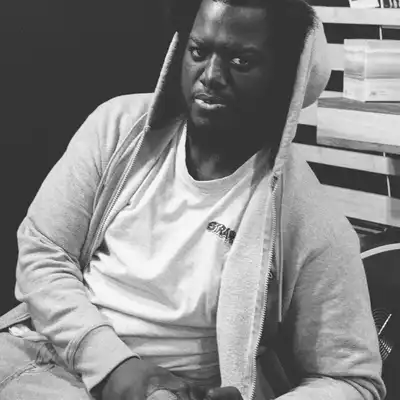 Black-and-white portrait of a man in a grey hoodie sitting on a stool in a studio