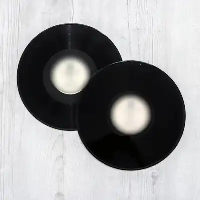 Two black vinyl records with plain labels lying on whitewashed boards