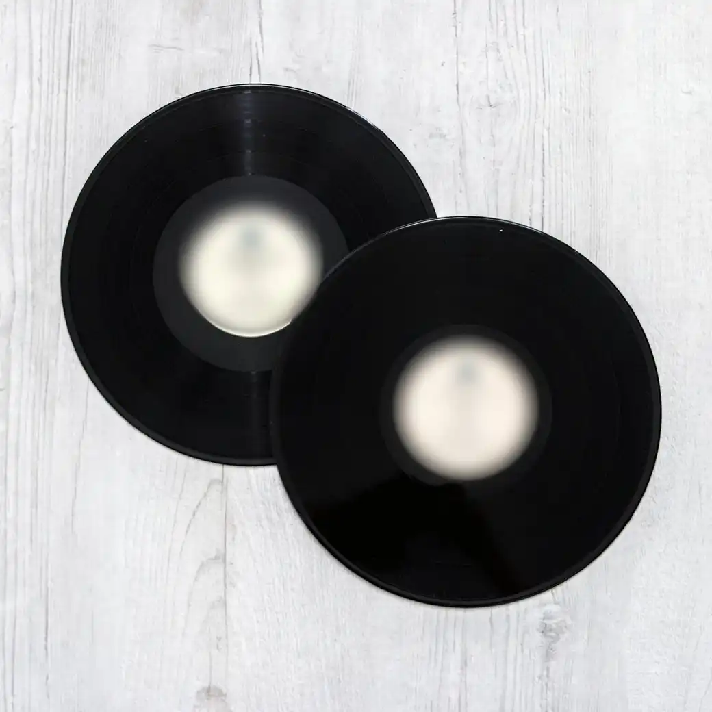 Two black vinyl records with plain labels lying on whitewashed boards
