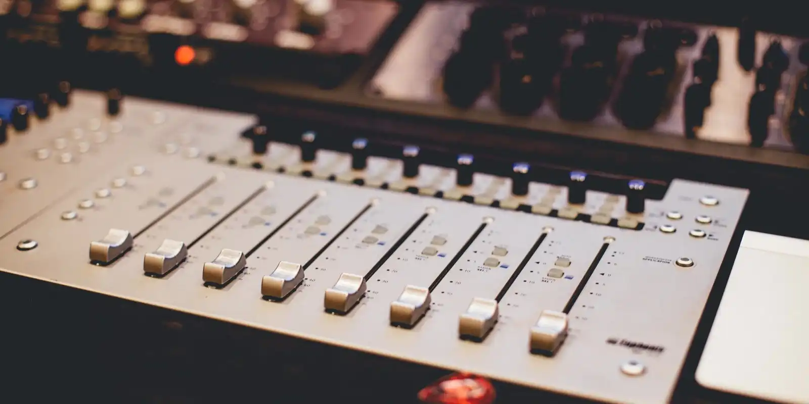 Faders and knobs of a studio mixing desk lit by small coloured lights