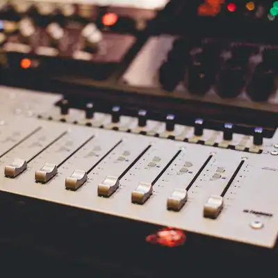 Faders and knobs of a studio mixing desk lit by small coloured lights